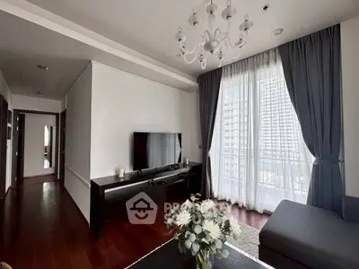 Elegant living room with chandelier, large TV, and floor-to-ceiling windows opening to a balcony.