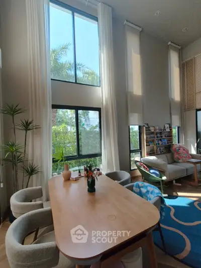 Spacious living room with high ceilings and large windows offering a serene garden view.