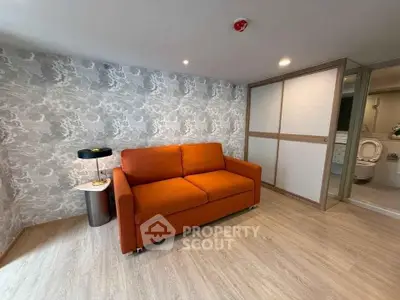 Modern living room with orange sofa and stylish wallpaper, featuring sliding door to bathroom.