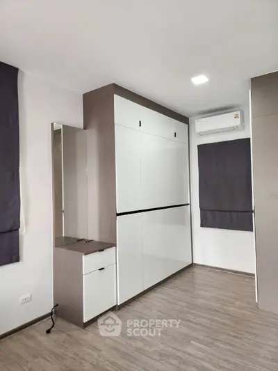 Modern bedroom with sleek wardrobe and air conditioning unit, featuring minimalist design and neutral tones.