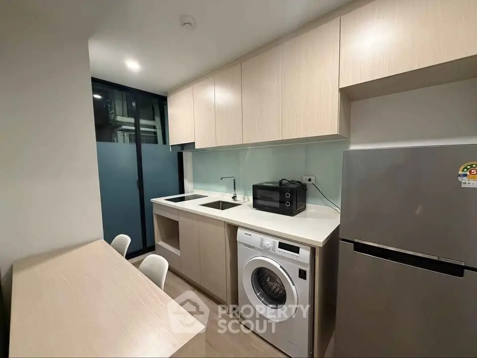 Modern kitchen with sleek cabinetry, washing machine, and stainless steel fridge in a compact layout.