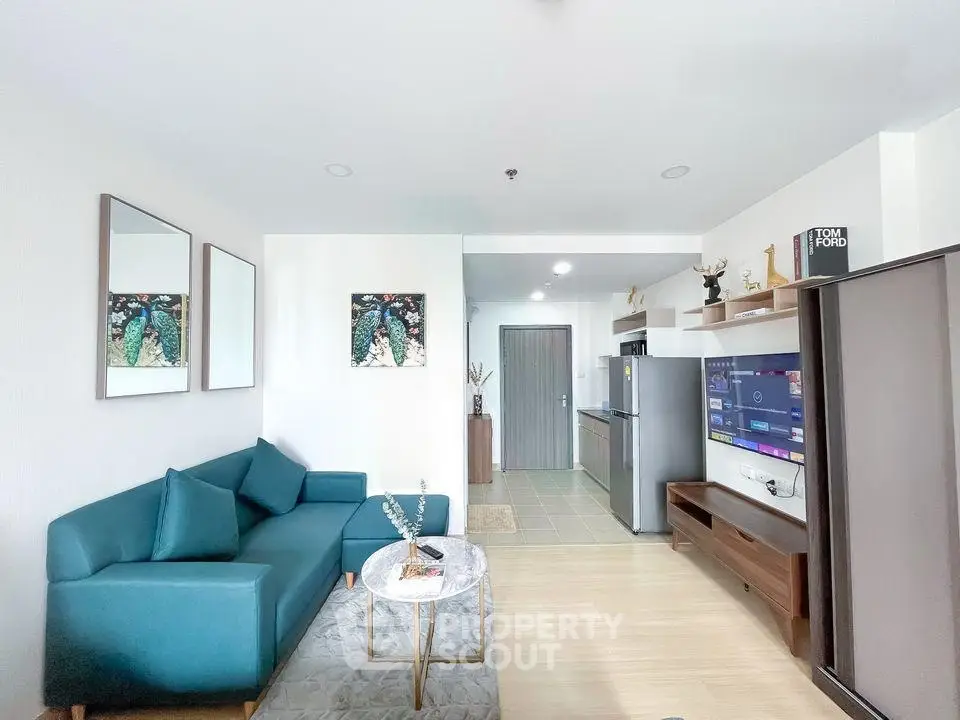 Modern living room with teal sofa, wall art, and open kitchen layout in stylish apartment.