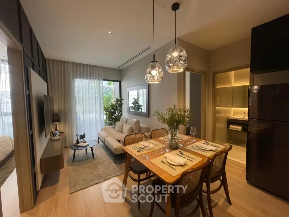 Elegant open-plan living space with modern furniture, chic pendant lights, and a seamless transition to a well-equipped kitchen, perfect for entertaining.