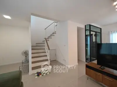 Modern living room with staircase and TV, featuring sleek design and neutral tones.