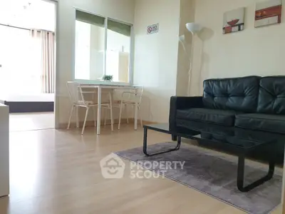 Modern living room with black leather sofa and glass coffee table in bright apartment.