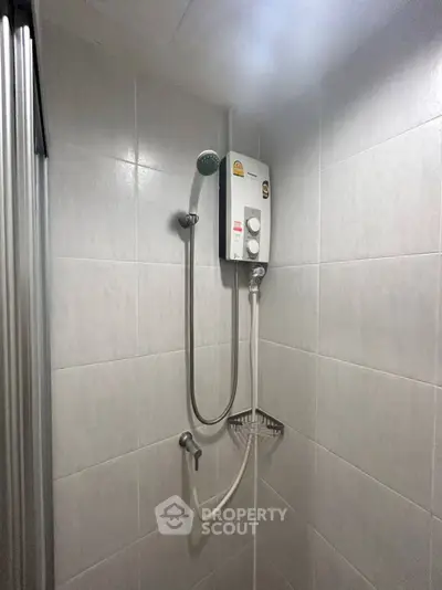 Compact bathroom shower area with electric water heater and tiled walls.