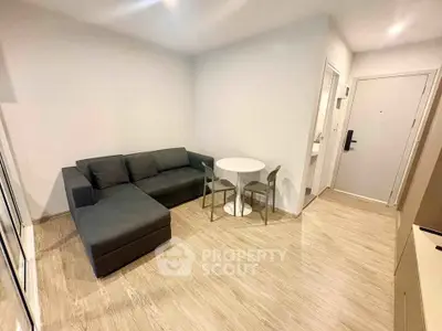 Modern living room with sleek gray sofa and compact dining area in stylish apartment.