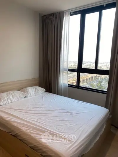 Cozy bedroom with large window offering stunning city view and natural light.