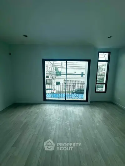 Spacious room with large window and balcony view, featuring elegant wooden flooring.