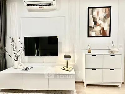 Modern living room with sleek white furniture and abstract art, featuring a wall-mounted TV and stylish decor.