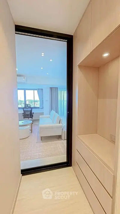 Modern apartment hallway leading to a bright living room with large windows and stylish furniture.