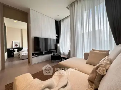Modern living room with cozy sectional sofa and large TV, leading to a stylish bedroom.