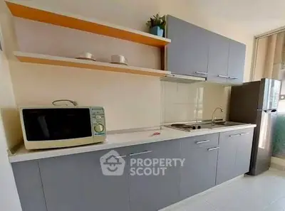 Modern kitchen with sleek cabinets, microwave, and compact fridge in a bright apartment.