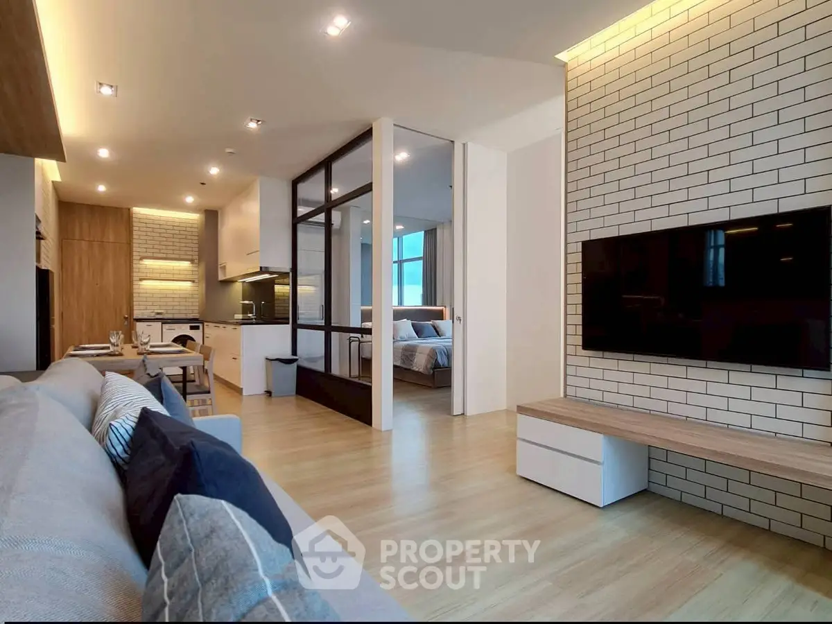 Modern open-plan living room with stylish decor and large TV, featuring a view into a cozy bedroom.