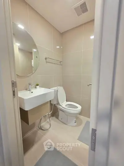 Modern bathroom with sleek fixtures and neutral tiles, featuring a round mirror and compact design.