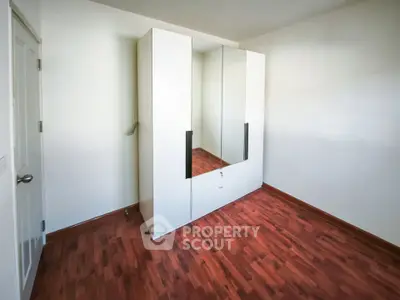Spacious bedroom with sleek wardrobe and polished wooden flooring