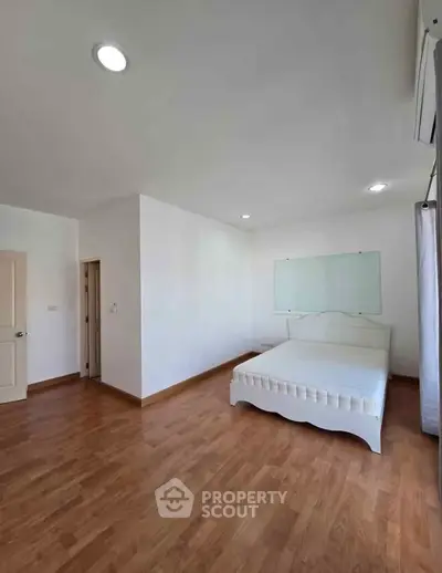 Spacious bedroom with wooden flooring and natural light, featuring a minimalist bed and neutral decor.