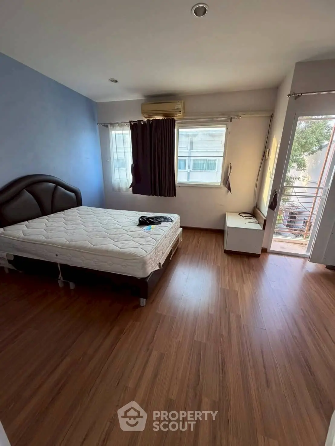 Spacious bedroom with wooden flooring and large windows offering natural light.
