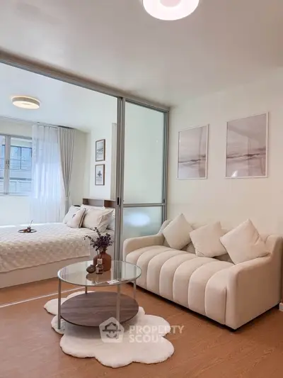 Modern living room with cozy sofa and glass coffee table, adjacent to a stylish bedroom with natural light.