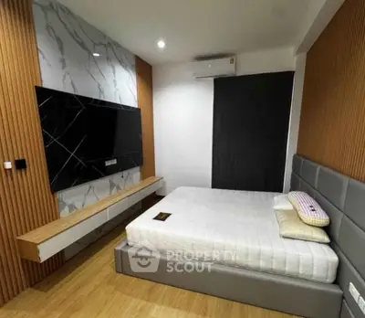 Modern bedroom with stylish decor and wall-mounted TV, featuring a comfortable bed and sleek wooden flooring.