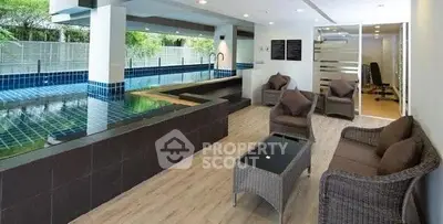 Luxurious indoor pool area with modern seating and fitness room view.
