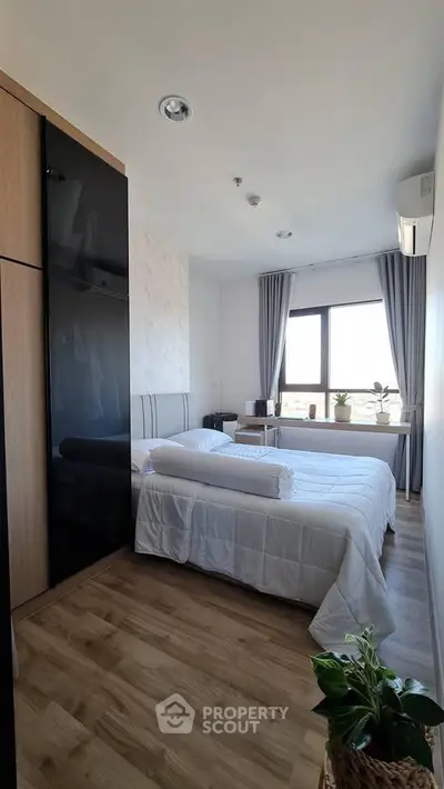 Modern bedroom with large window and stylish decor, featuring wooden flooring and natural light.