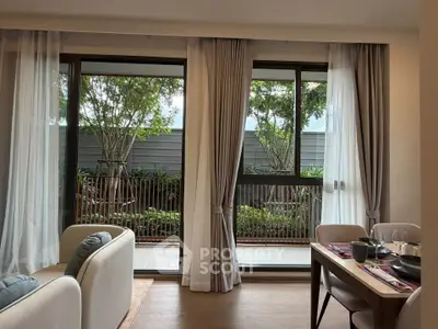 Elegant living room with large windows opening to a lush garden view, featuring cozy seating and dining area.