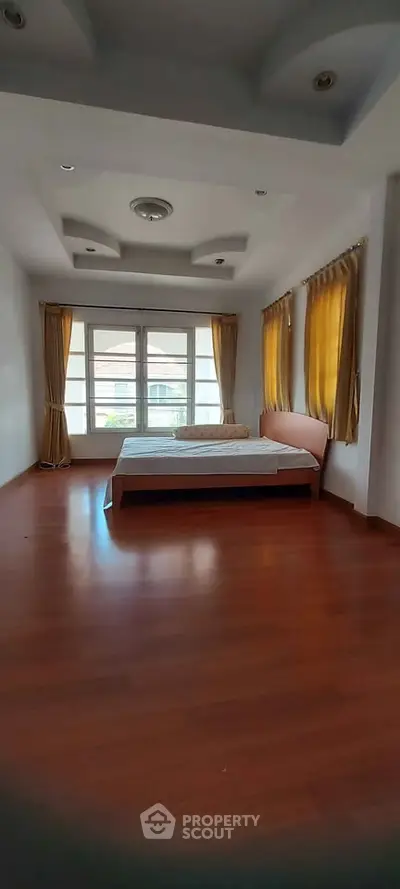 Spacious bedroom with large windows and wooden flooring, offering ample natural light and elegant curtains.