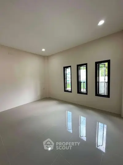 Spacious empty room with glossy tiled floor and large windows, perfect for customization.