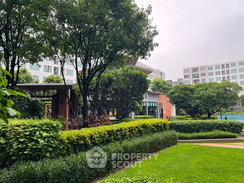 Lush green garden with modern apartment buildings in the background, offering serene living environment.