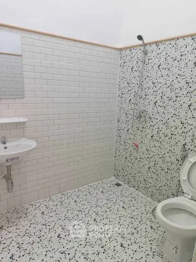 Modern bathroom with white subway tiles and terrazzo flooring, featuring a shower and toilet.