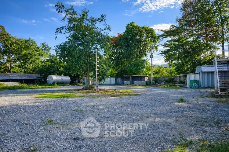 Spacious outdoor area with gravel surface, surrounded by lush greenery and utility structures, ideal for development.