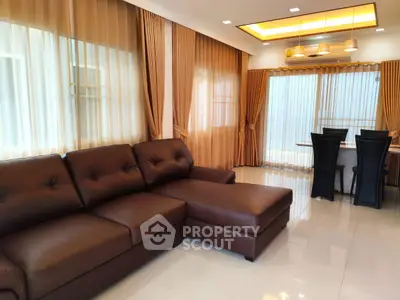 Luxurious living room with elegant brown leather sofa and dining area, featuring floor-to-ceiling curtains.