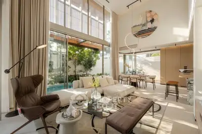 Luxurious living room with high ceilings and pool view, featuring modern furniture and elegant decor.