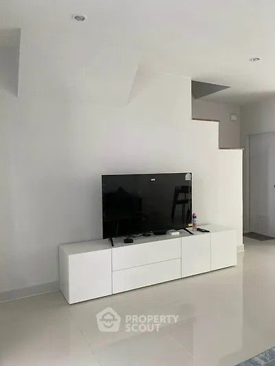 Modern living room with sleek white TV stand and flat-screen TV, showcasing minimalist design.