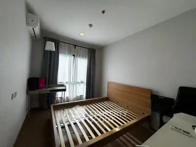 Modern bedroom with wooden bed frame, desk, and natural light from large window.