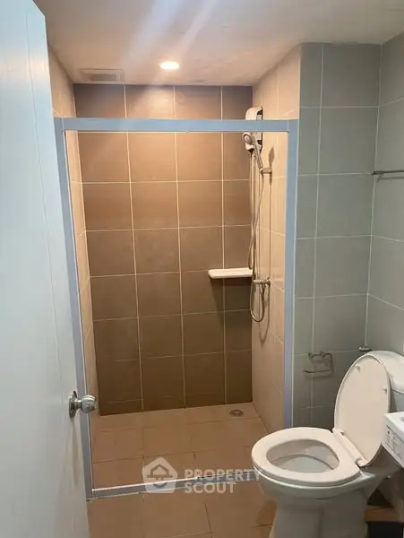 Modern bathroom with walk-in shower and toilet in a sleek tiled design.
