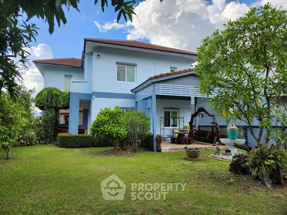 Charming blue two-story house with lush garden and patio seating area.