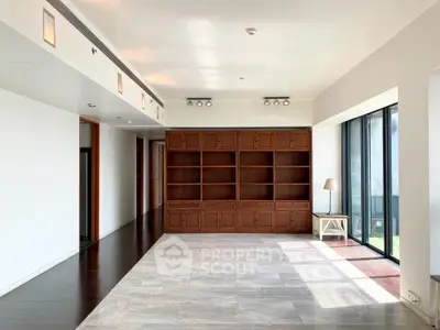 Spacious living room with built-in wooden shelves and large windows offering natural light.