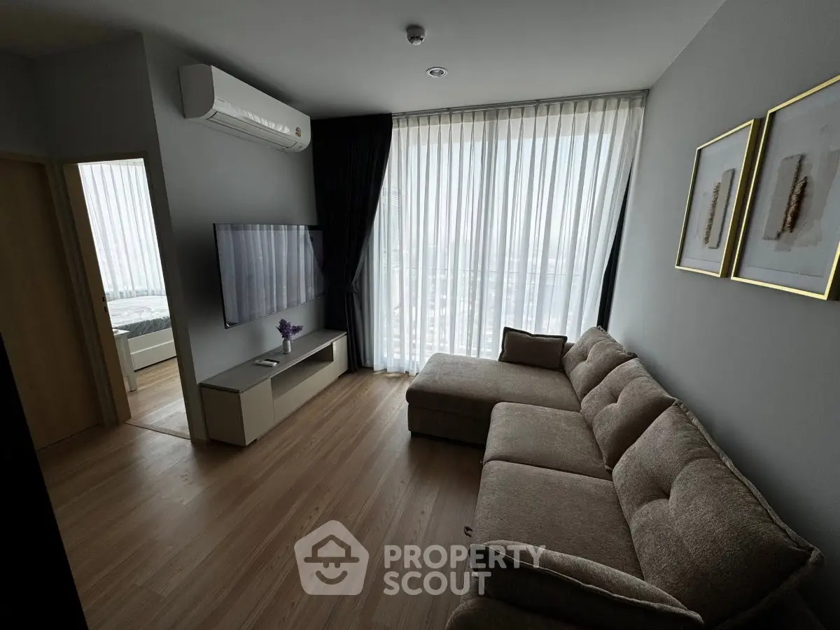 Modern living room with large window, cozy sofa, and wall-mounted TV in a stylish apartment.