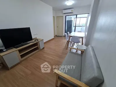 Modern living room with sleek furniture and wooden flooring, featuring a TV and dining area.