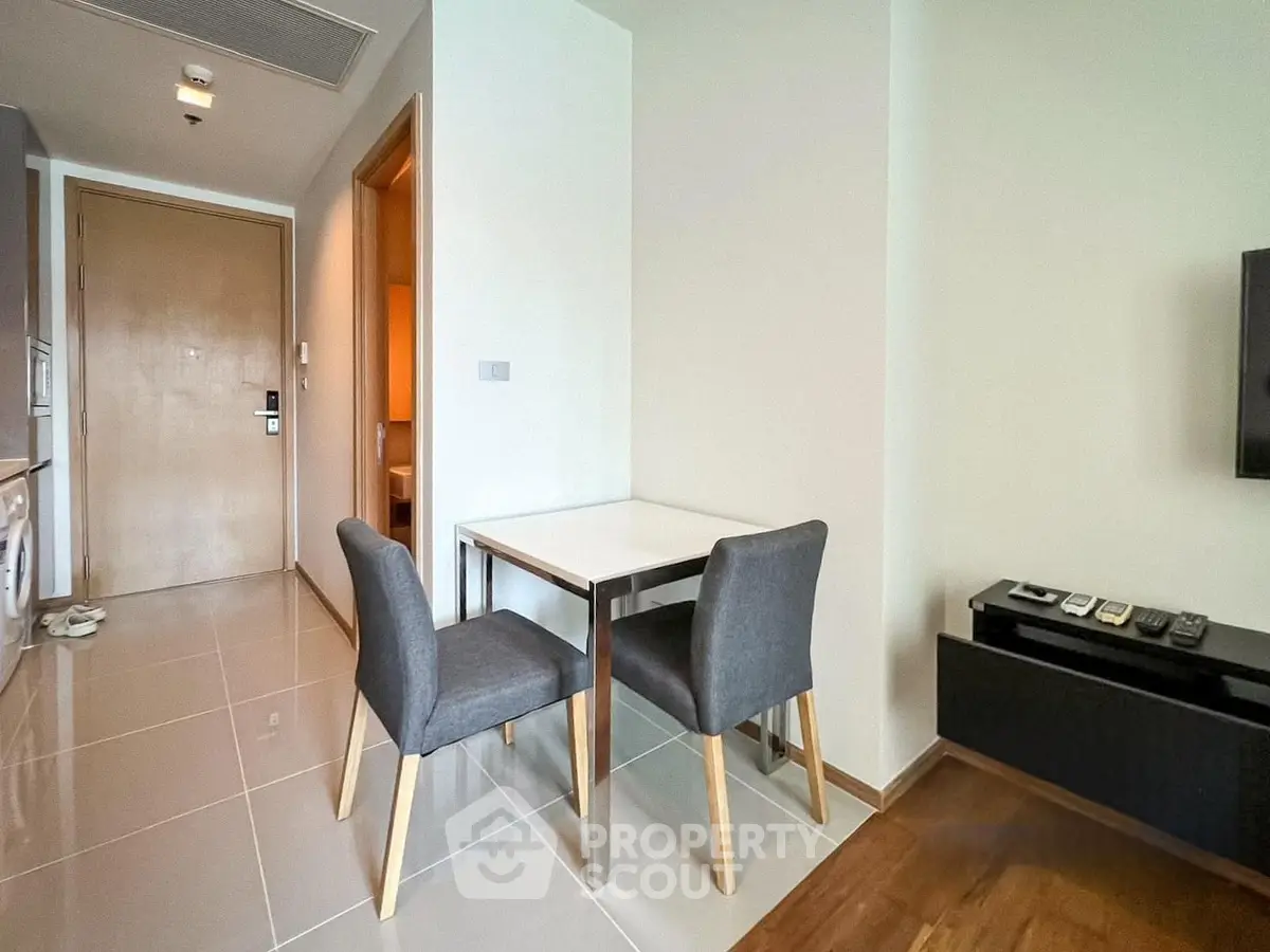 Modern apartment interior with dining area and TV setup, featuring sleek furniture and neutral tones.