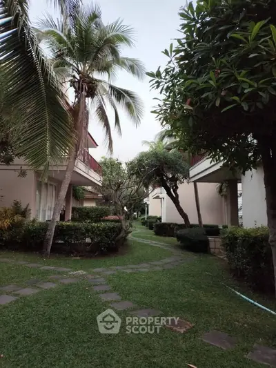 Charming garden view of residential complex with lush greenery and palm trees, perfect for serene living.