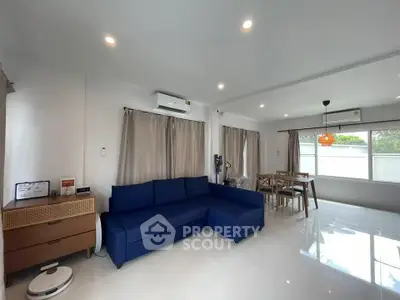 Spacious modern living room with blue sofa and dining area, bright natural light