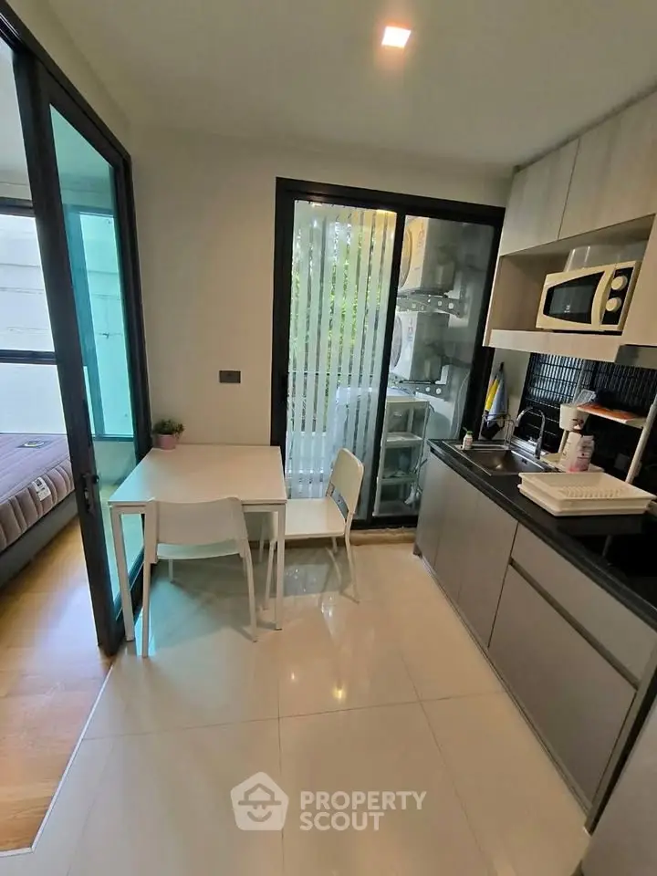 Modern compact kitchen with dining area and view into bedroom, featuring sleek cabinetry and appliances.
