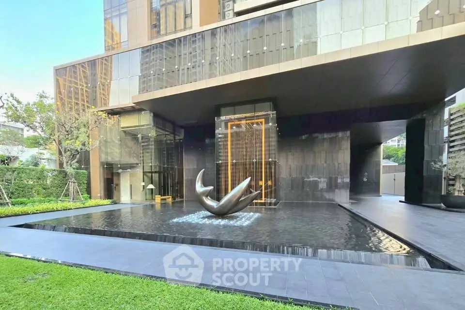 Luxurious modern building entrance with elegant water feature and lush greenery.