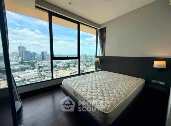 Spacious bedroom with stunning city view from large windows in modern high-rise apartment.