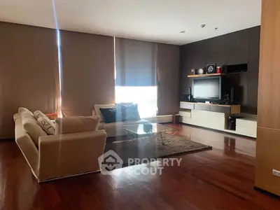 Spacious modern living room with sleek furniture and entertainment center, featuring warm wooden flooring.