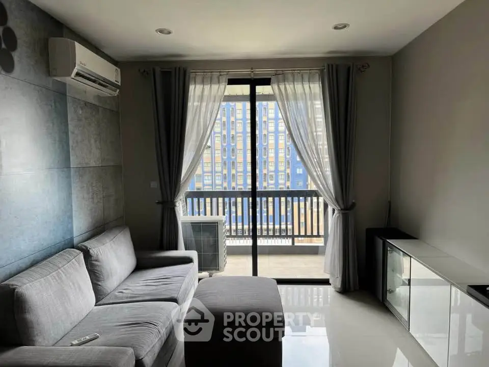 Modern living room with balcony view, featuring sleek gray sofa and air conditioning unit.