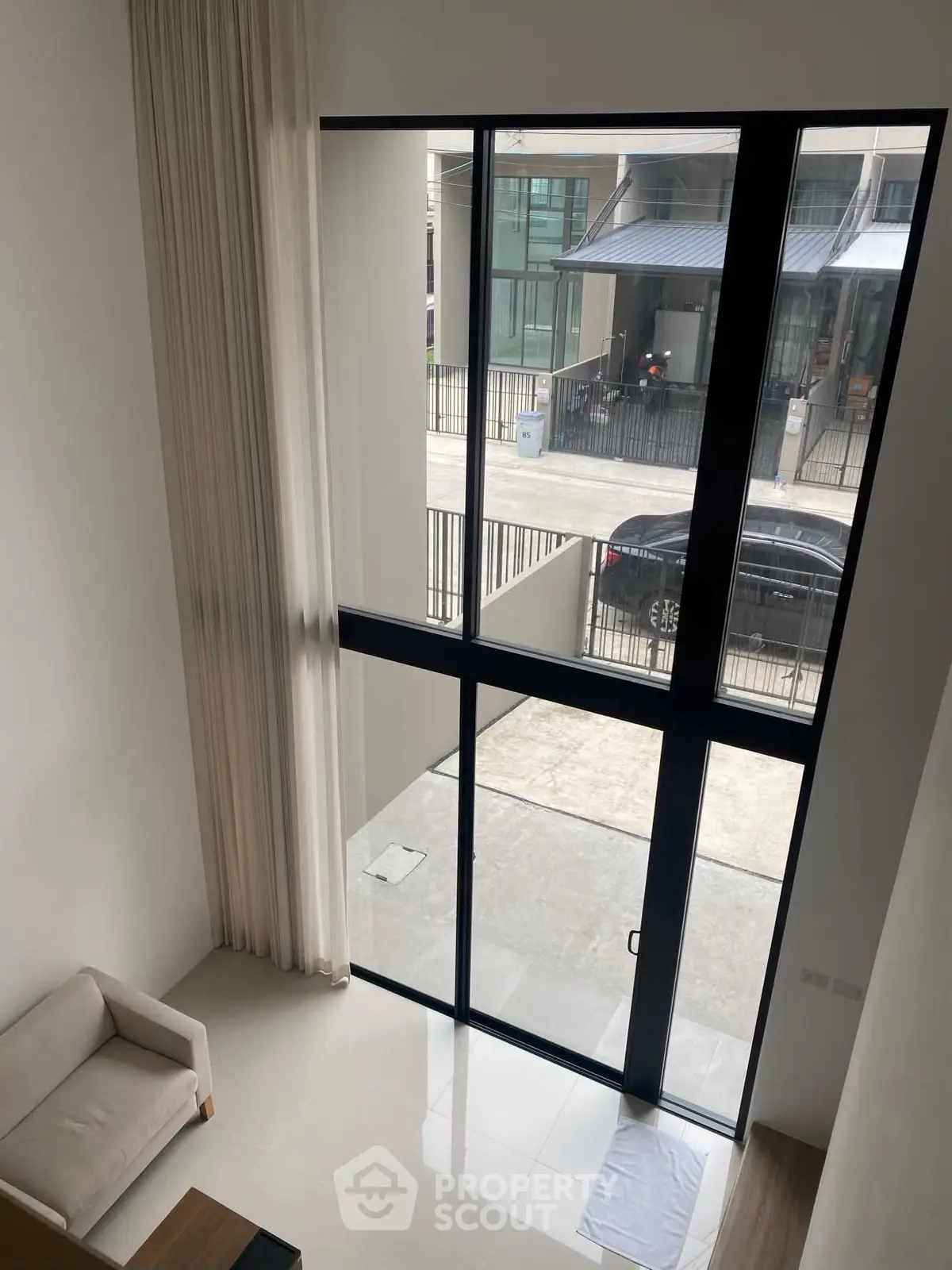 Spacious modern living room with floor-to-ceiling windows and elegant curtains, offering abundant natural light.